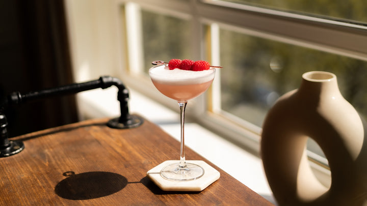 Pink cocktail presented in the NUDE hepburn glass in a scenery next to the window
