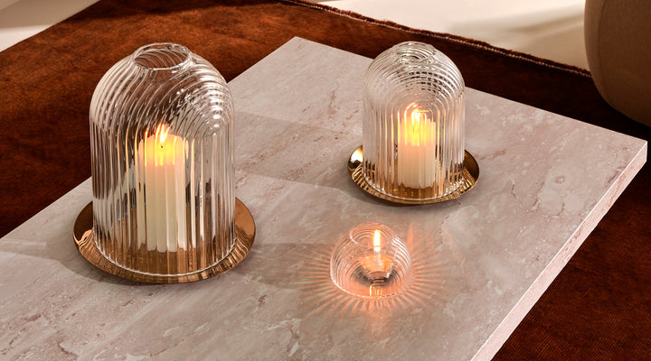 Rippled, clear leadfree glass domes on copper plates, functioning like candle holders in 2 sizes and a small votive holder. Presented on a marble table with candles lit.