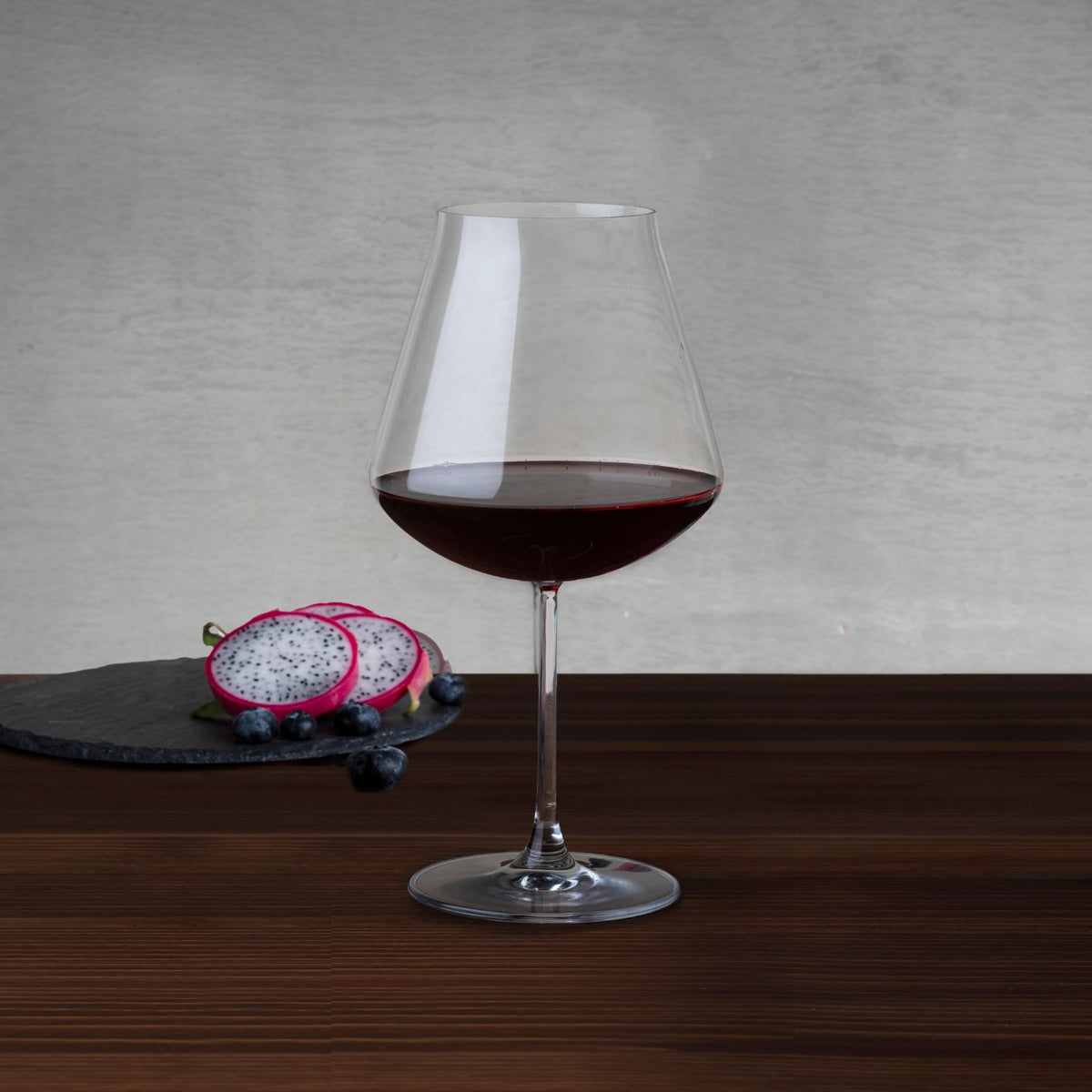 NUDE Salute Burgundy wine glass filled with red wine, beside dragon fruit and blueberries on a slate board