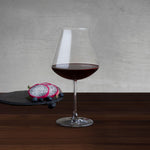 NUDE Salute Burgundy wine glass filled with red wine, beside dragon fruit and blueberries on a slate board