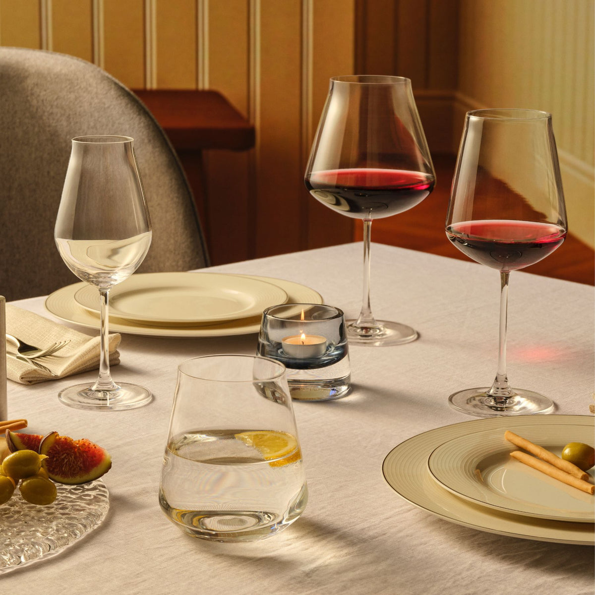 NUDE Salute wine glasses and tumbler on a set dining table with Joy votive candle, plates and olives
