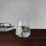 NUDE Salute tumbler with water, ice and lemon slice beside a book and reading glasses on a wooden table