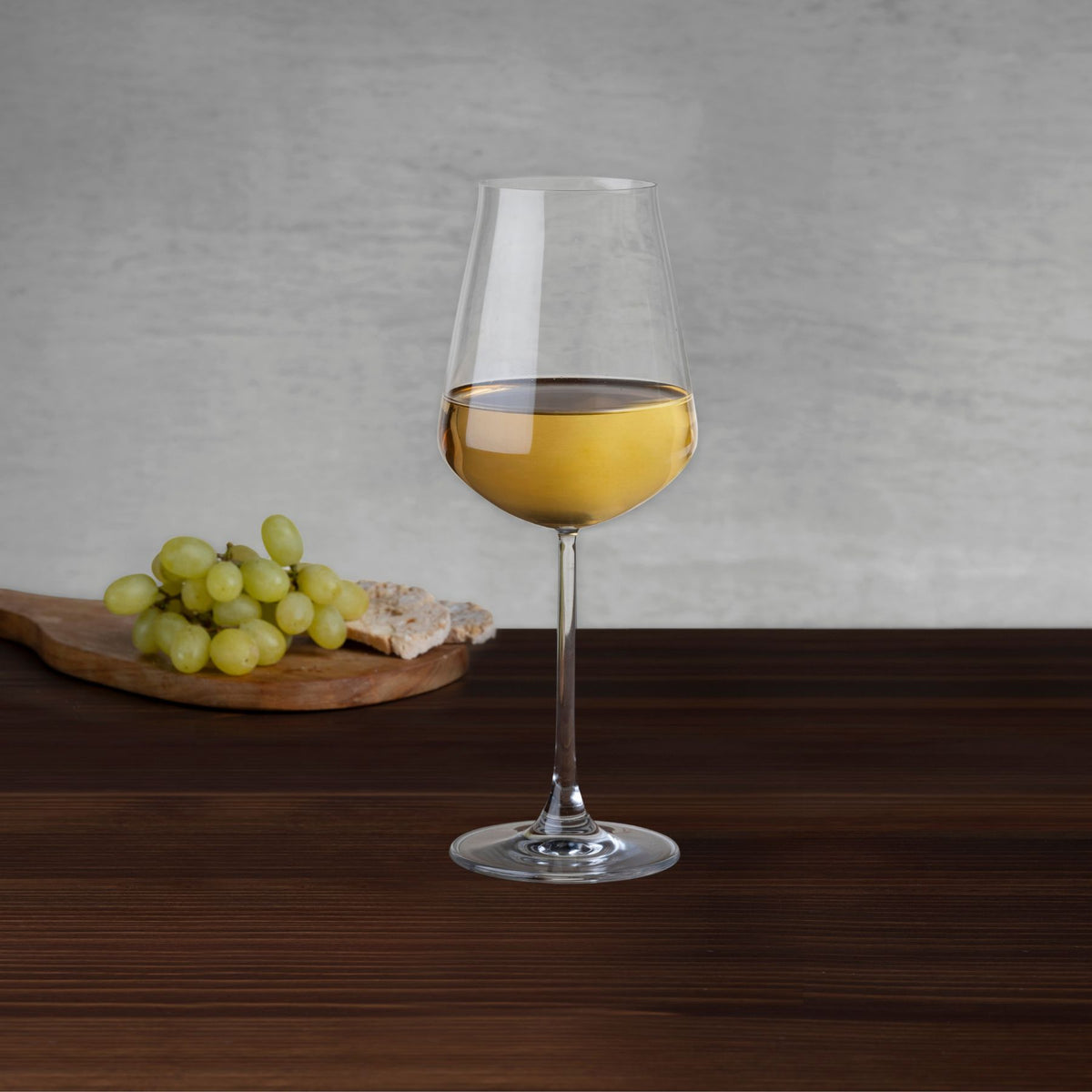 NUDE Salute white wine glass with white wine beside green grapes and bread on a wooden board
