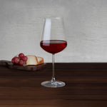 NUDE Salute red wine glass with red wine beside aged cheese and red grapes on a wooden board