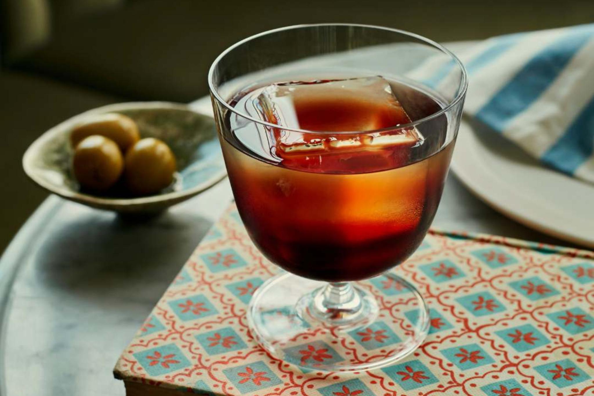 NUDE Bar/giani cocktail glass short holding an old-fashioned on a green velvet banquette
