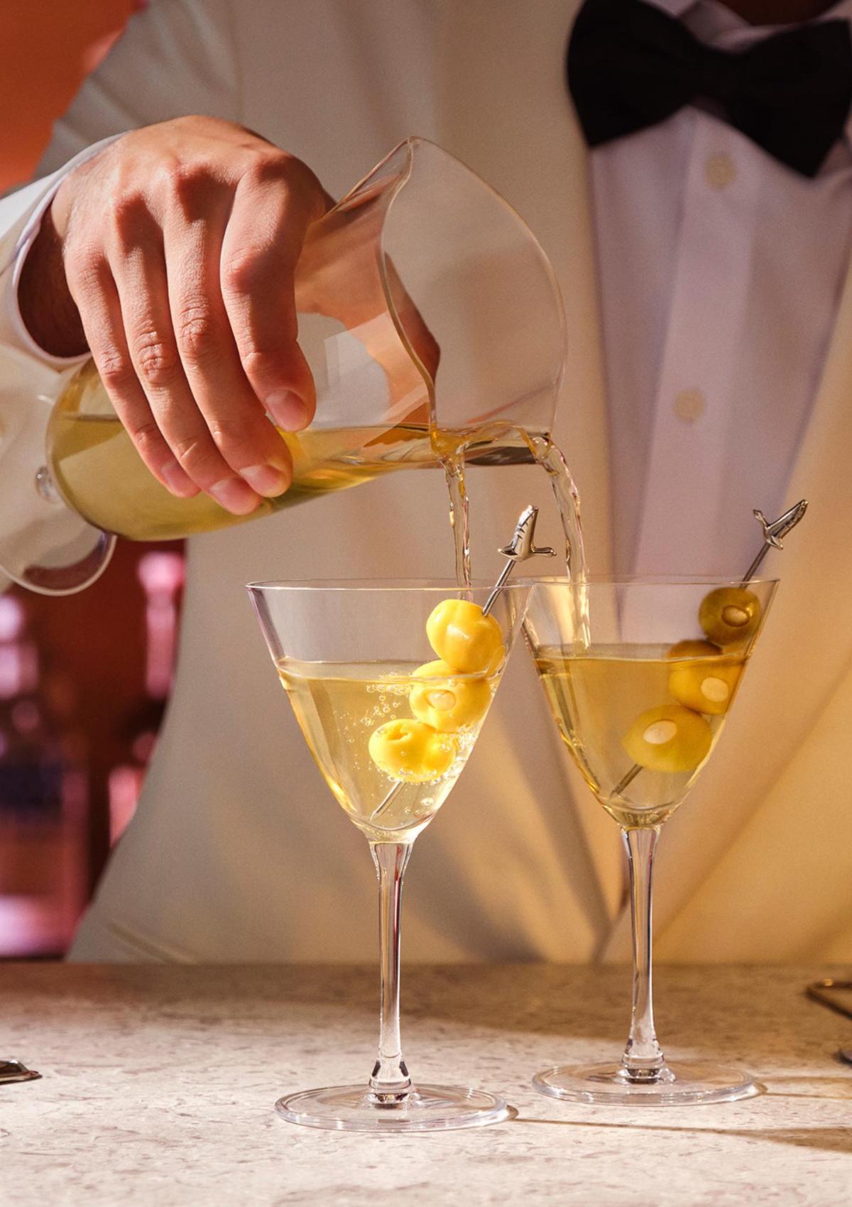 A bartender in a white dinner jacket pouring two martinis at once from the NUDE Bar/Giani Double Pour Mixing Glass