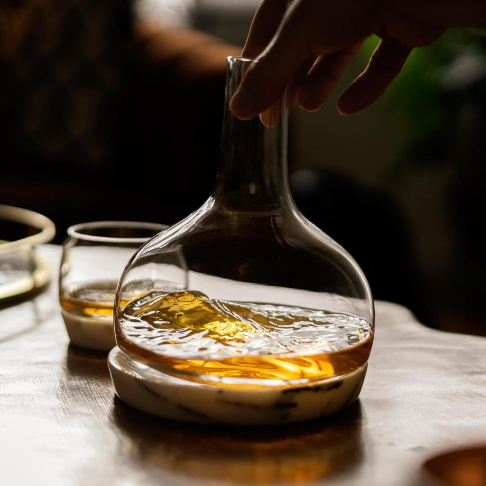 Hand tilting a NUDE Chill whisky decanter on a marble coaster