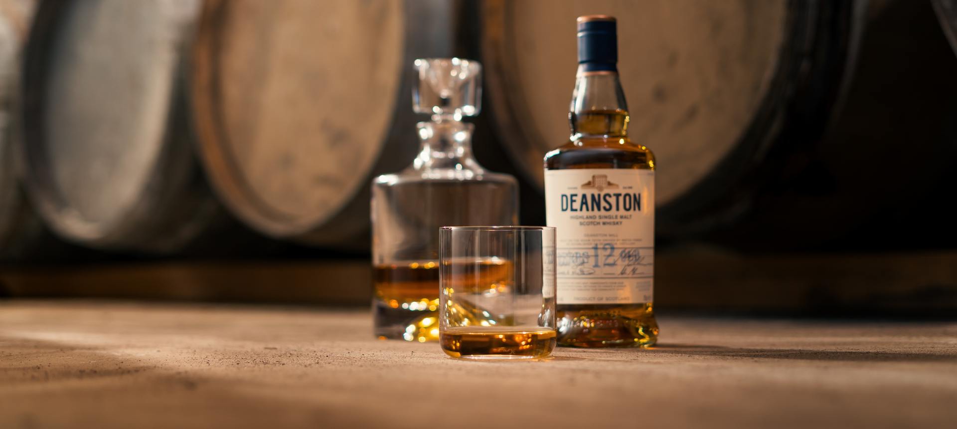 NUDE Finesse decanter and whisky glasses with Deanston 12 Year Highland Single Malt Scotch Whisky in front of oak barrels, photography by Murray Anderson