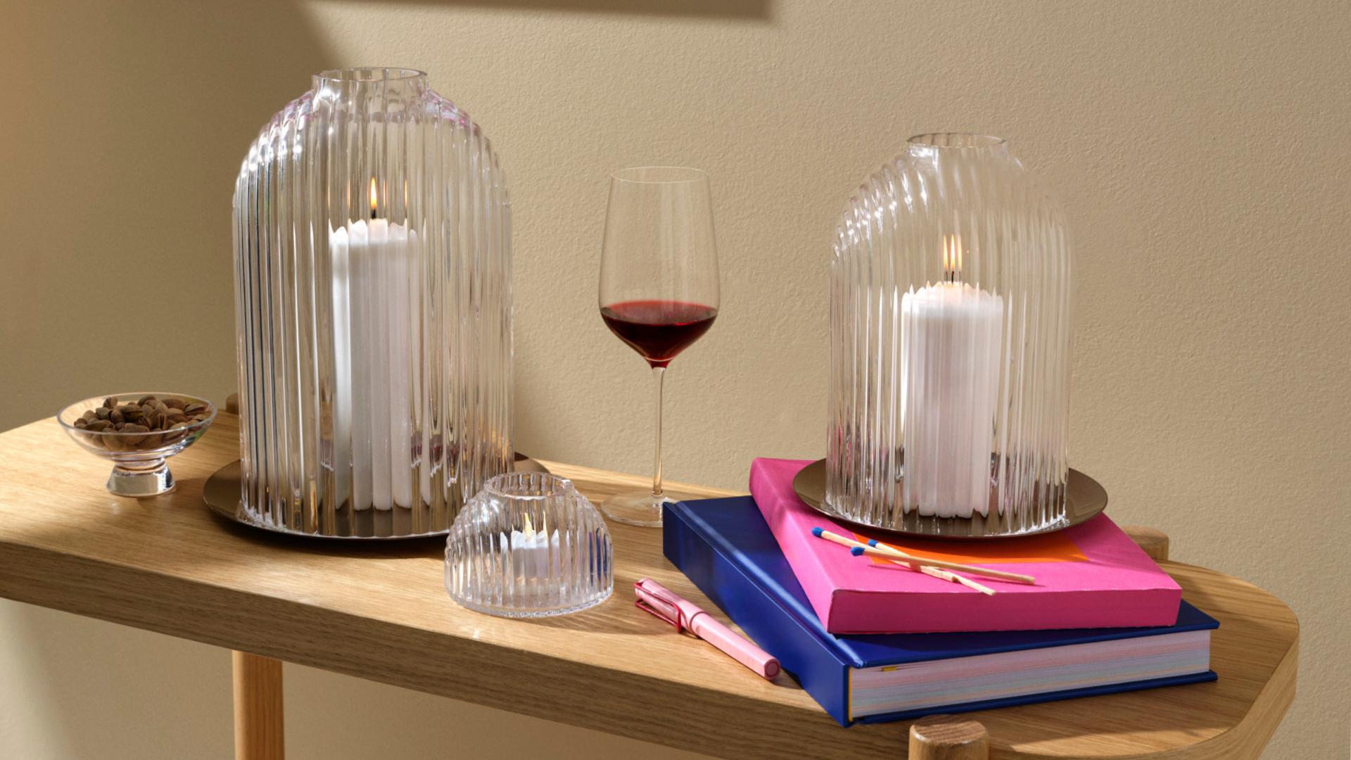 NUDE Ilo candleholders in two sizes with votive tealight holder and Stem Zero wine glass styled on oak console with colorful books.