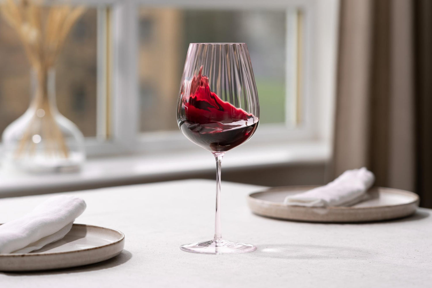  Red wine swirling in a NUDE Round Up Dusty Rose Red Wine Glass on a table by a window