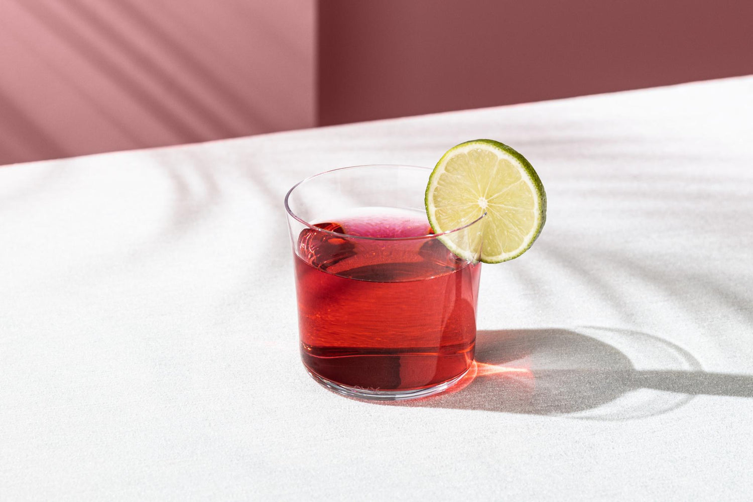NUDE Savage Low Ball Glass with a red cocktail and lime wheel on a blush backdrop.
