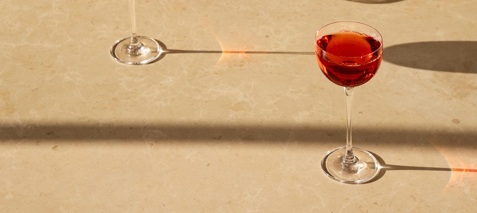 NUDE Savage Pony glass holding a red cocktail on a sunlit marble surface