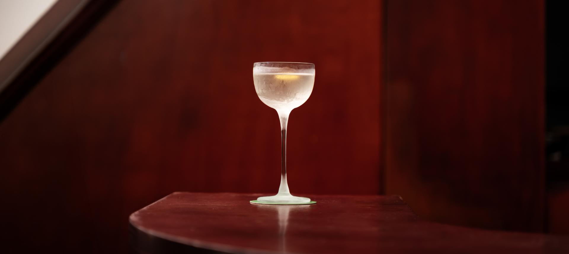 A frosted NUDE Savage Pony Glass backlit on dark wood, with the words "Everything tastes better when served in a good-looking glass" — Rémy Savage.