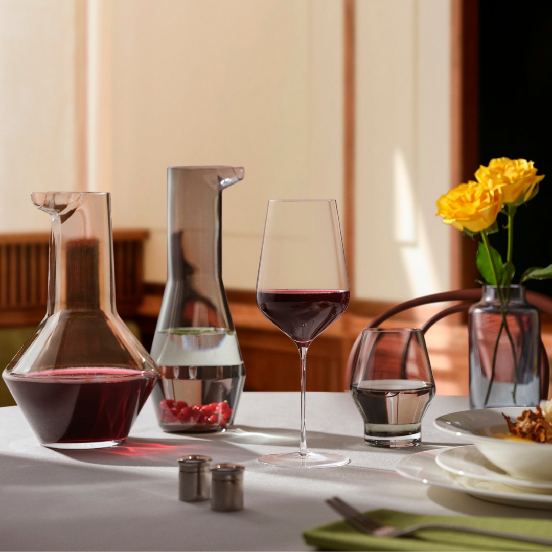 NUDE Stem Zero Masterglass with red wine on a fine dining table setting with Beak water carafe, smoke tumbler and yellow roses