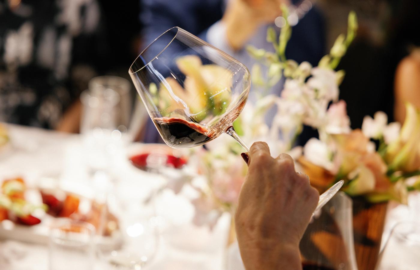 Hand swirling red wine in a NUDE Stem Zero Vertigo Elegant Red Wine Glass Medium at an elegant New York dinner table