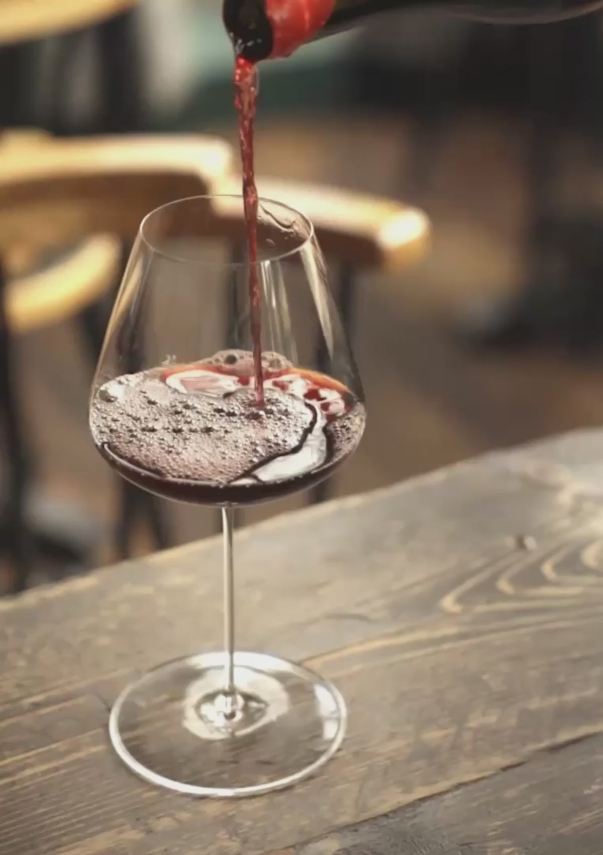 Honey Spencer pouring red wine into a NUDE Stem Zero glass at a sunlit restaurant table